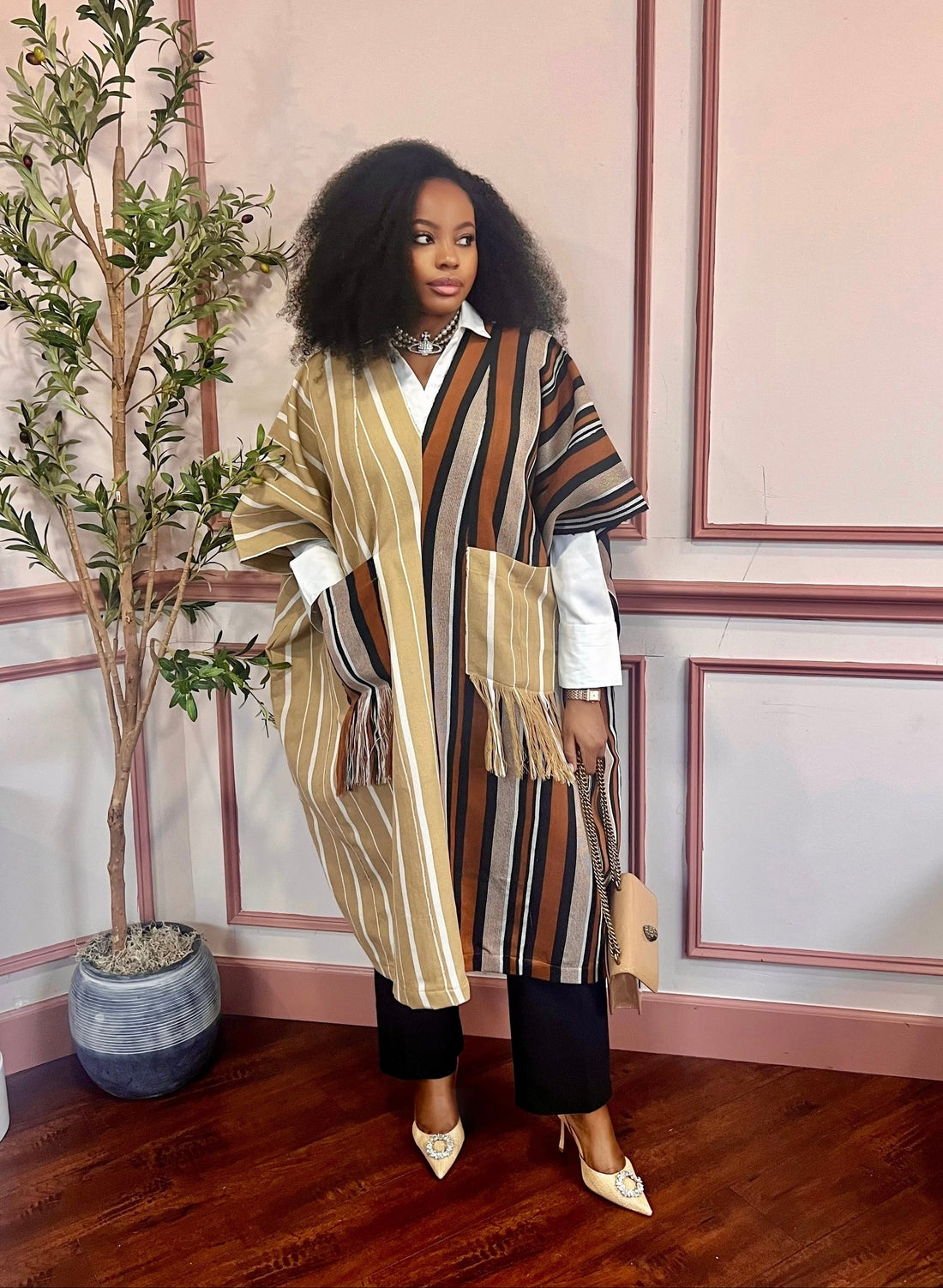 Woman styling the striped handwoven Aṣọ Òkè Adunni kaftan over a white blouse and black trousers.